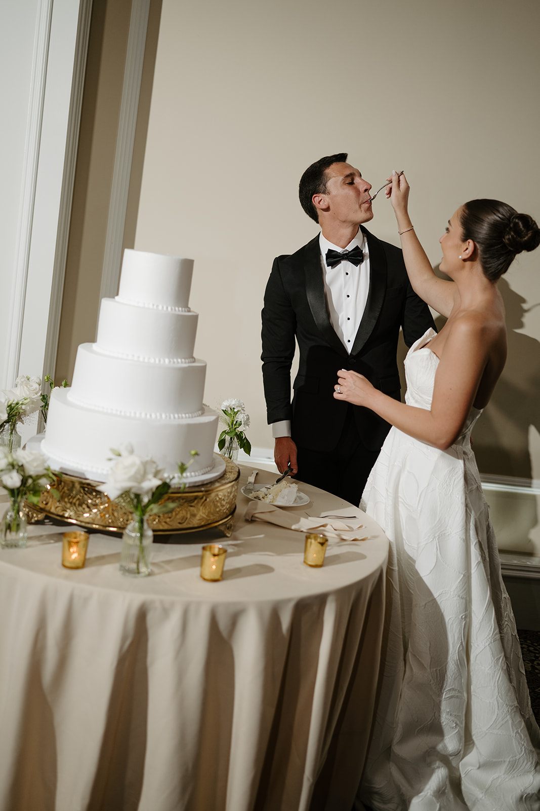 Bride feeding the groom a forkful of wedding cake at their reception cake table.